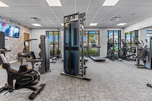 Ein modernes Fitnessstudio mit Cardiogeräten, Krafttrainingsgeräten und großen Fenstern mit Blick auf Palmen.