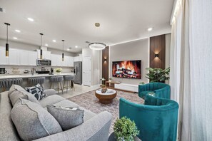 This stylish living area features a plush gray sofa and vibrant teal chairs, creating a striking contrast. Enjoy cozy movie nights with the wall-mounted TV above a sleek entertainment unit, all set in a warmly lit atmosphere. - 5BR townhouse at Windsor Cay Resort (Clermont)