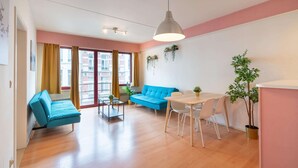 Een moderne woonkamer met een bank, eettafel, stoelen en een hangplant.