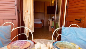 A room with a bed, a TV, and a dining area with a table set for two. - New Orange Studio Apartment in Limpiddu, Budoni – Pool, Terrace, Wi-Fi (Budoni)