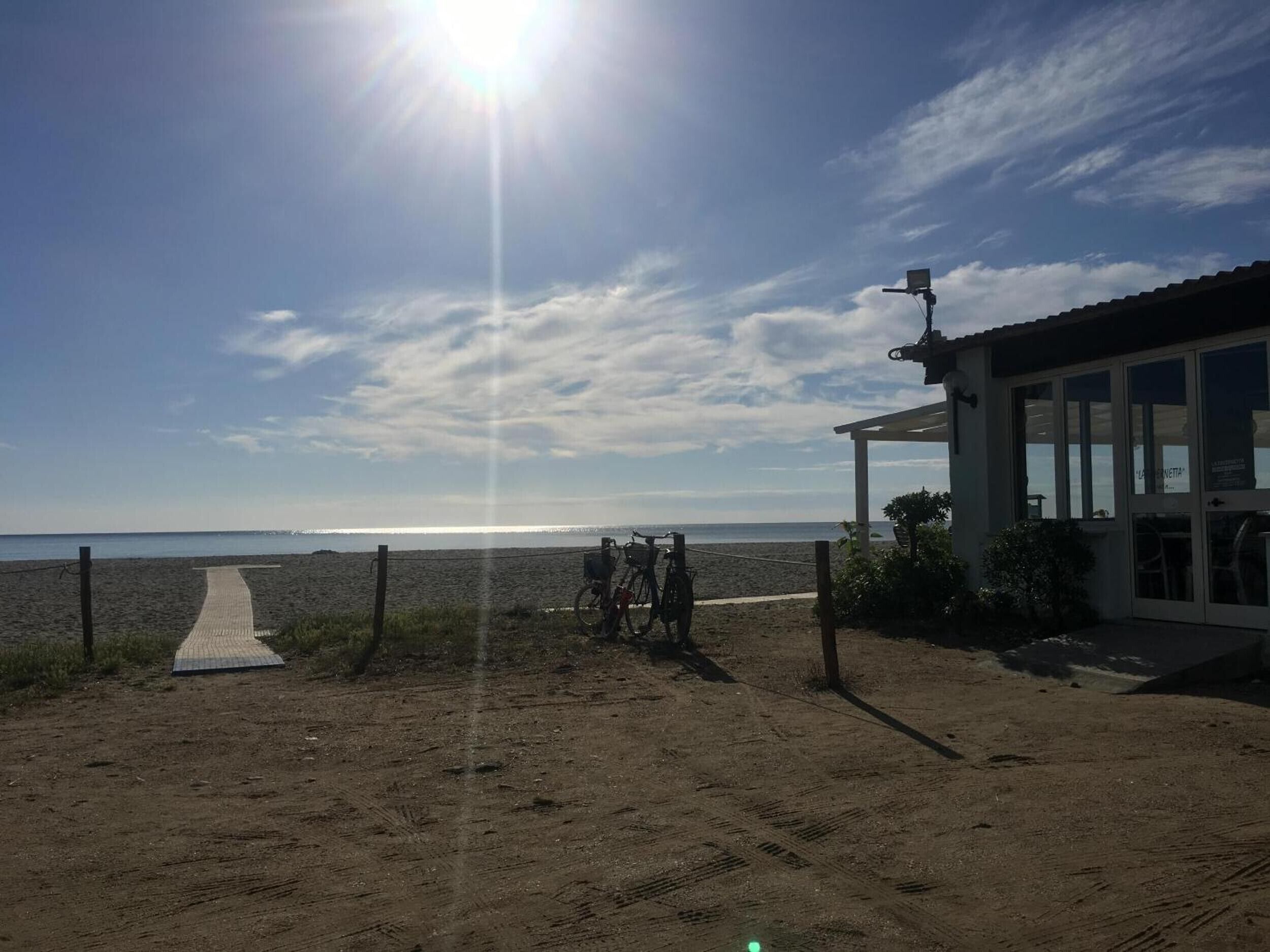 Vista de la playa con un camino que lleva a un edificio con amplias ventanas.