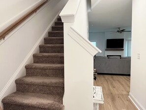 Eine Treppe führt zu einem Wohnbereich mit Deckenventilator und Flachbildfernseher.
