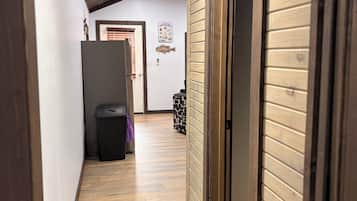 A hallway with wooden flooring, a door on the right, and a trash bin in the center.