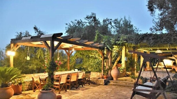 Un'area patio esterna con pavimento in pietra, pergola in legno e piante in vaso.