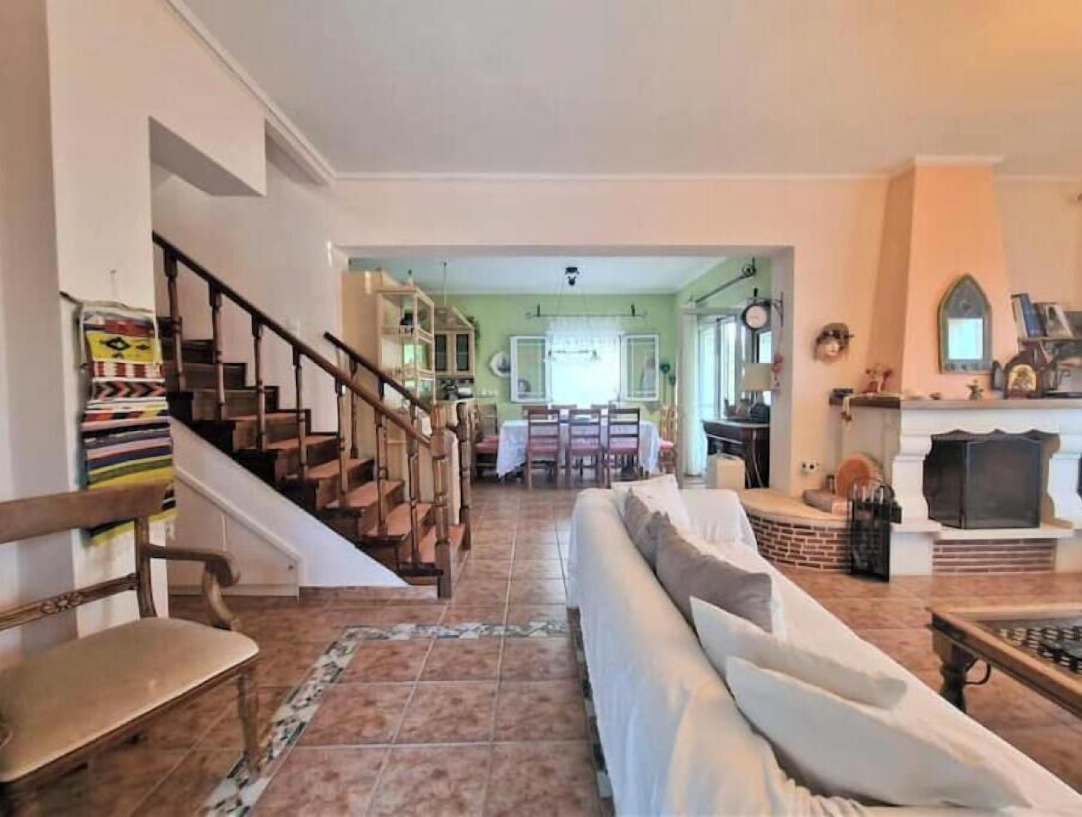 A living room with a sofa, a TV, a fireplace, a staircase, and a dining area.