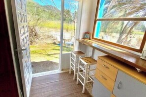 Ein Zimmer mit einem Holztisch, einem Fenster mit Gartenblick und einer zur Außenseite führenden Tür.