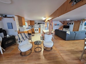 A modern kitchen with wooden cabinets, a dining area with a table and chairs, a gray sofa, and a small round table with two chairs.