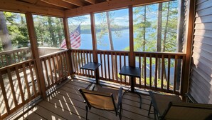 A wooden deck with a view of a lake and trees, featuring a table and chairs. - 3-Bedroom House on Beautiful Flying Pond in Mt. Vernon, ME (Mount Vernon)