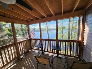 A wooden deck with a view of a lake and trees, featuring a table and chairs.