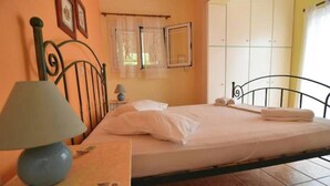 Un dormitorio con cama, mesita de noche con lámpara, ventana con cortinas y armario.