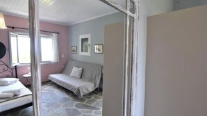 A room with a stone floor, a bed, a sofa, a window, and framed pictures on the wall. - Sweet Studio with Amazing Sea View (Zakynthos)