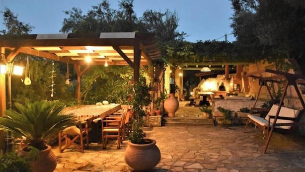An outdoor patio area with stone flooring, wooden furniture, potted plants, and a pergola structure. - Sweet Studio with Amazing Sea View (Zakynthos)