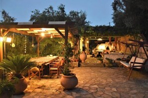 Eine Außenpatio-Terrasse mit Steinboden, Holzmöbeln, Kübelpflanzen und einer Pergola.