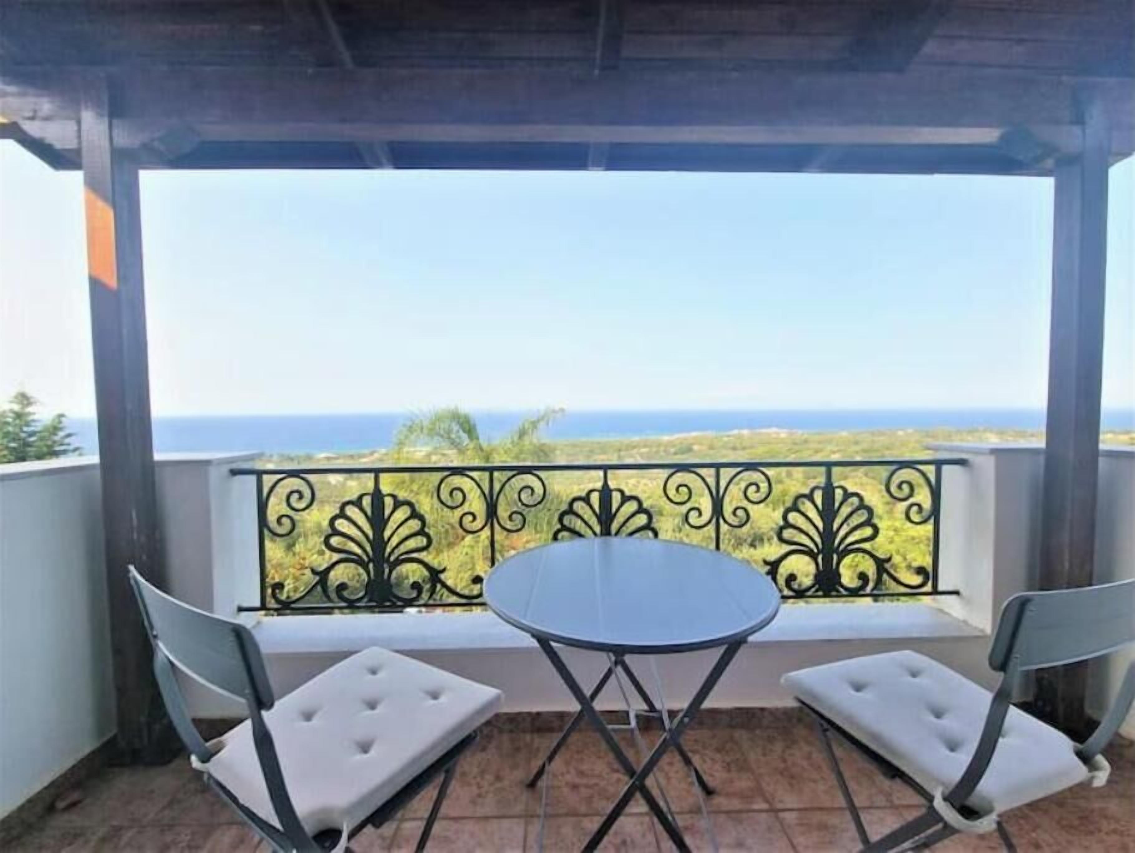 Ein Balkon mit Tisch und zwei Stühlen, der auf eine Küstenlandschaft blickt.