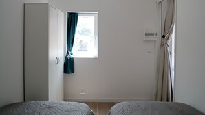 Un dormitorio con dos camas, una ventana con cortinas, un armario y una puerta.