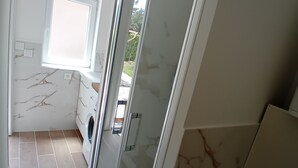 Un baño moderno con cabina de ducha de vidrio, lavadora integrada y un ventanal que proporciona luz natural.