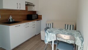 Cocina compacta con armarios blancos, microondas y un pequeño comedor con mesa y sillas.