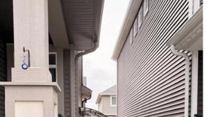 A narrow concrete pathway leading to a wooden gate, flanked by buildings with siding and a mailbox. - Private Suite w/ Full Kitchen Near Banff National Park (Cochrane)