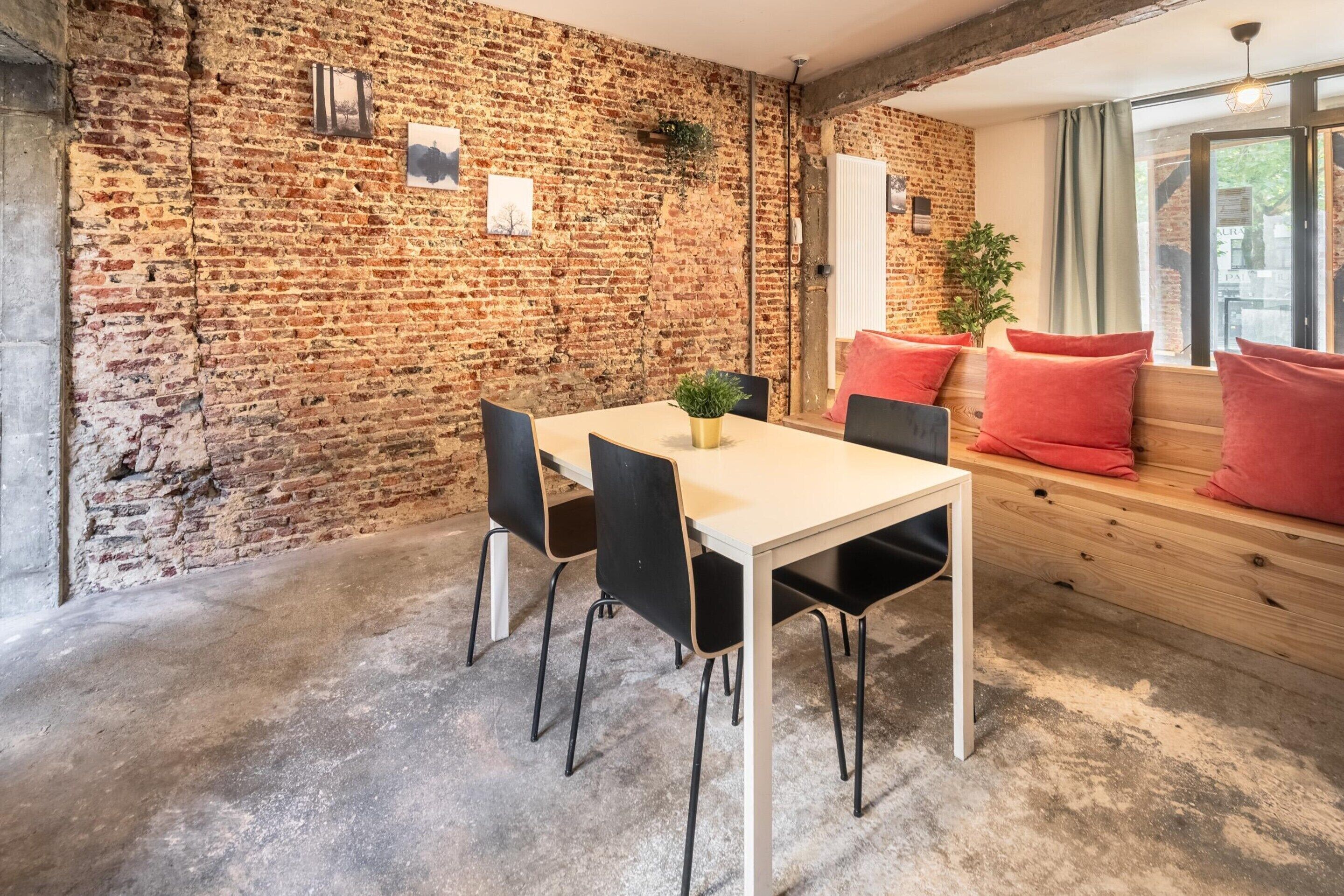 A room with a brick wall, a wooden bench, a table with chairs, and a potted plant.