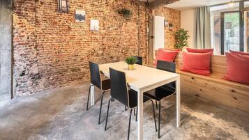 A room with a brick wall, a wooden bench, a table with chairs, and a potted plant.