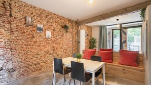 A room with a brick wall, a wooden bench with red cushions, a table with chairs, and a window with a view. - The Industrial Apartments 2bbknsinternet (Antwerp)