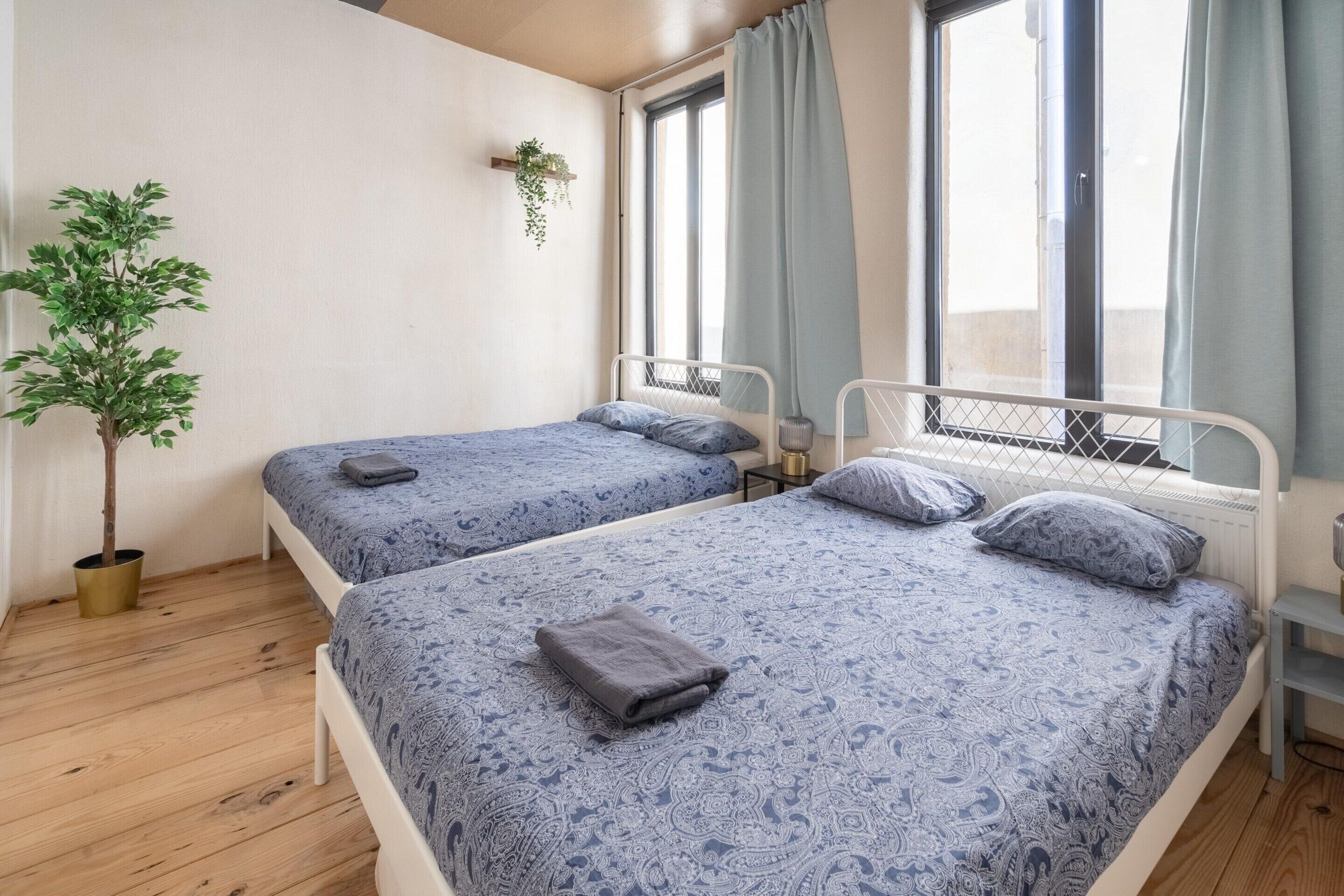 Une chambre avec deux lits, une plante en pot et une fenêtre avec des rideaux.