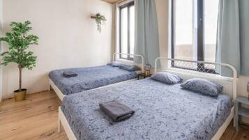Una habitación con dos camas, una planta en maceta y un ventanal con cortinas.