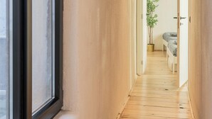 A narrow hallway with wooden flooring, a potted plant, and a bed in the distance. - The Industrial Apartments 2bbknsinternet (Antwerp)