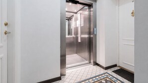 Ein moderner Aufzug mit Metalloptik, Fliesenboden und einer Tür mit Messinggriffen.