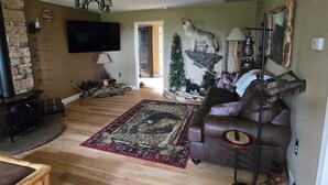 A living room with a fireplace, a television, a ceiling fan, a sofa, a rug, and a Christmas tree.