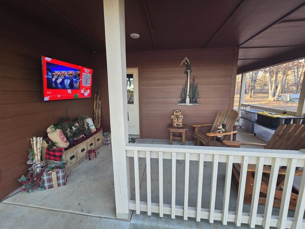A porch with a television, Christmas decorations, a wooden bench, and a view of the outdoors.