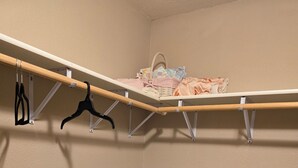 A corner of a room with a baby crib, a shelf with clothes, and a hanging rack with black hangers.