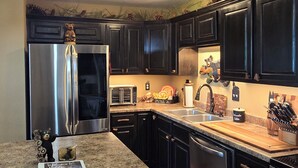 A kitchen with dark cabinets, stainless steel appliances, a granite countertop, and a bear figurine.