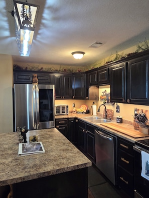 A kitchen with dark cabinets, stainless steel appliances, a granite countertop, and a bear figurine.