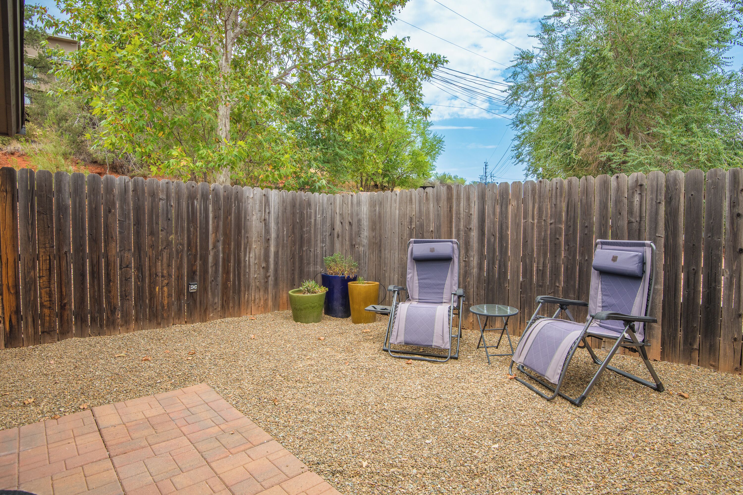 Un jardin avec une clôture en bois, deux chaises de jardin et trois plantes en pot.