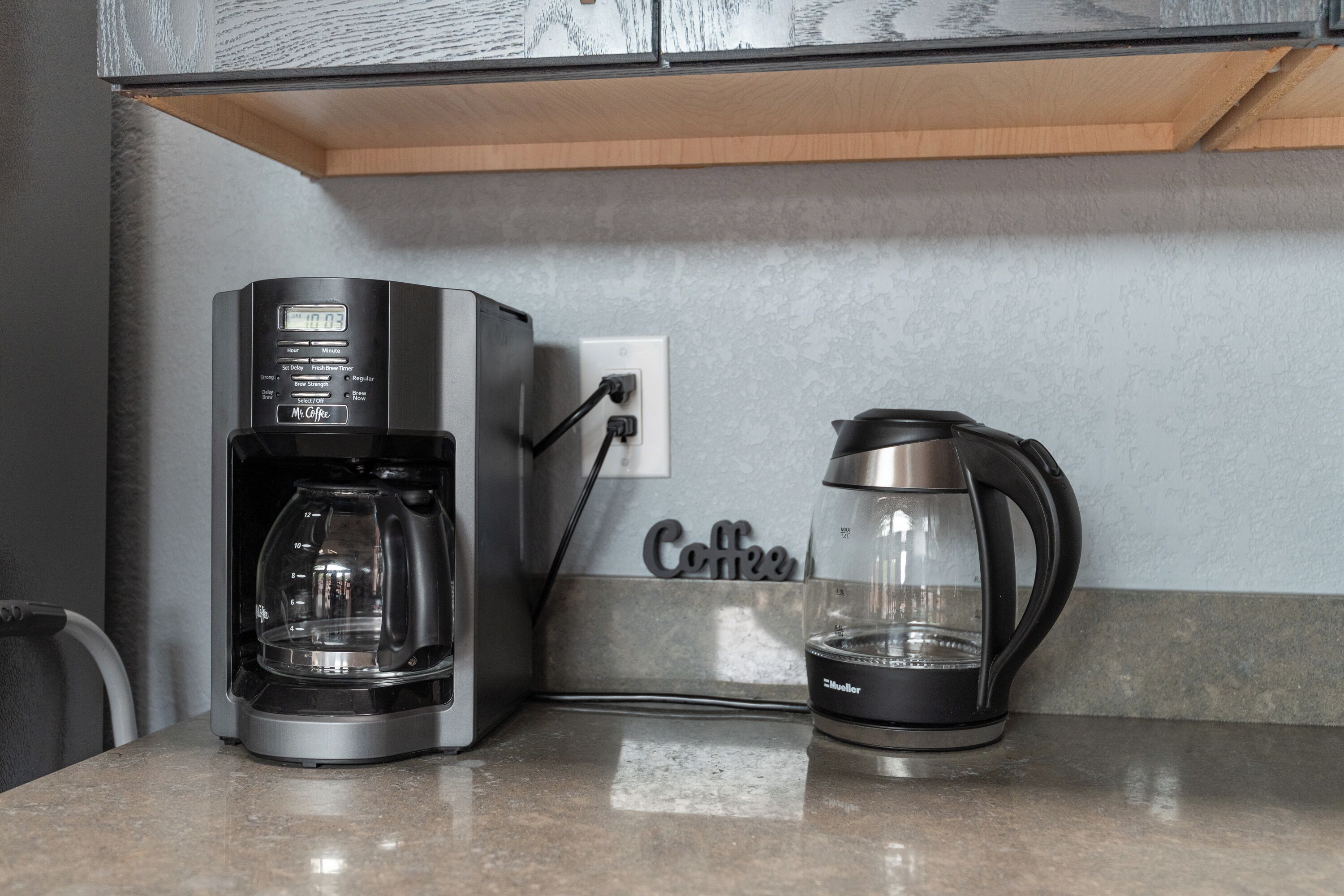 A coffee maker and a kettle on a countertop, connected to a power outlet.