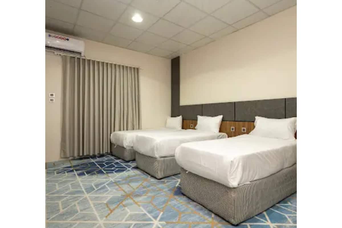 A hotel room with two beds, a large window with curtains, a patterned floor, and a ceiling with recessed lighting.