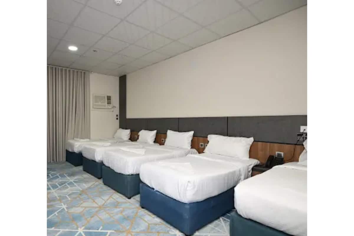 A hotel room with four beds arranged in a row, a large window with curtains, and a patterned floor.