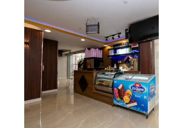 A modern hotel lobby with a reception desk, a food display, and a large screen. - Wardat rahiq (Madinah)