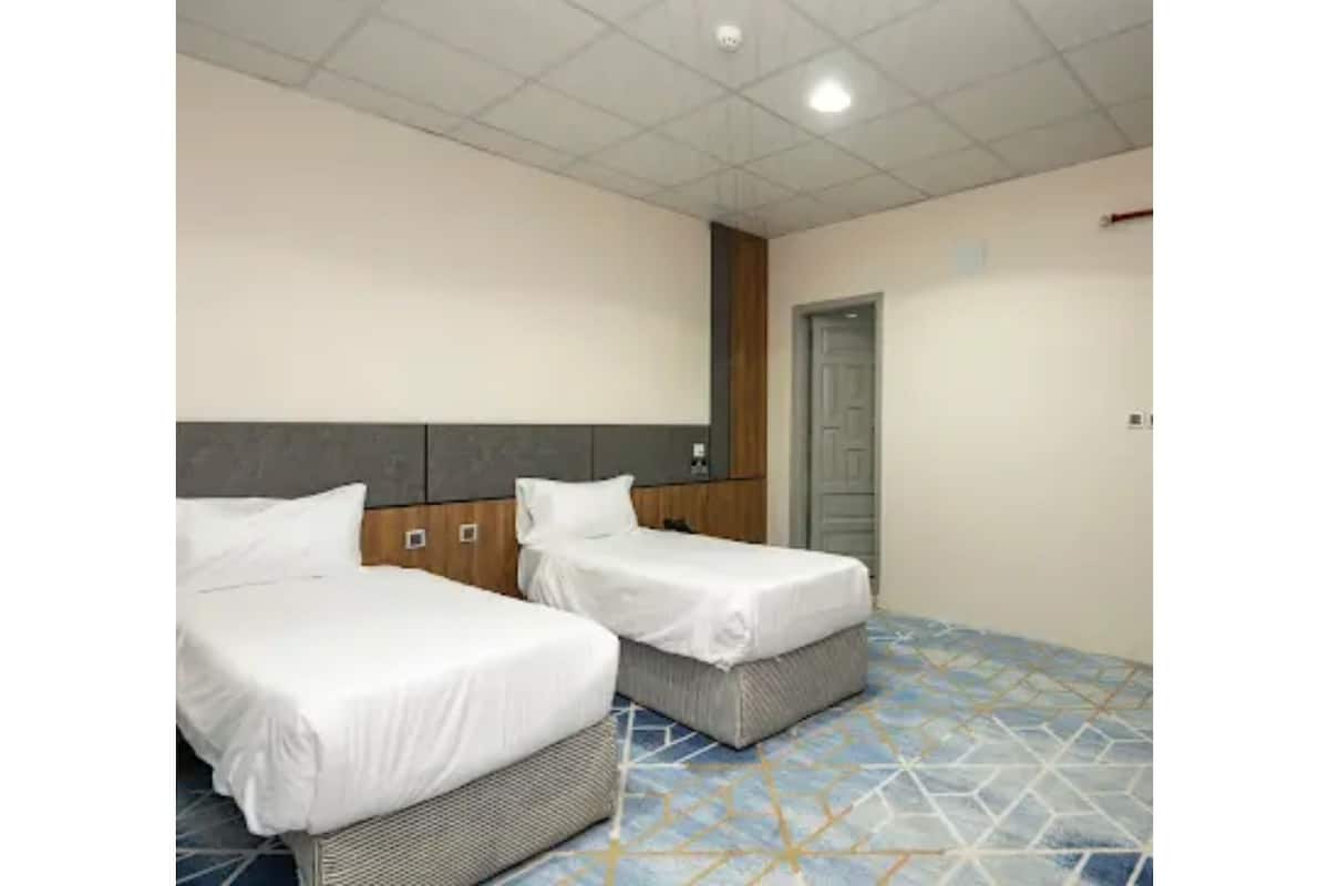 A room with two single beds, a tiled floor, a wooden headboard, and a door.