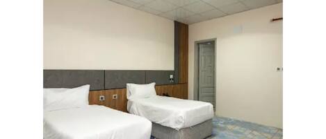 A room with two single beds, a tiled floor, a wooden headboard, and a door.