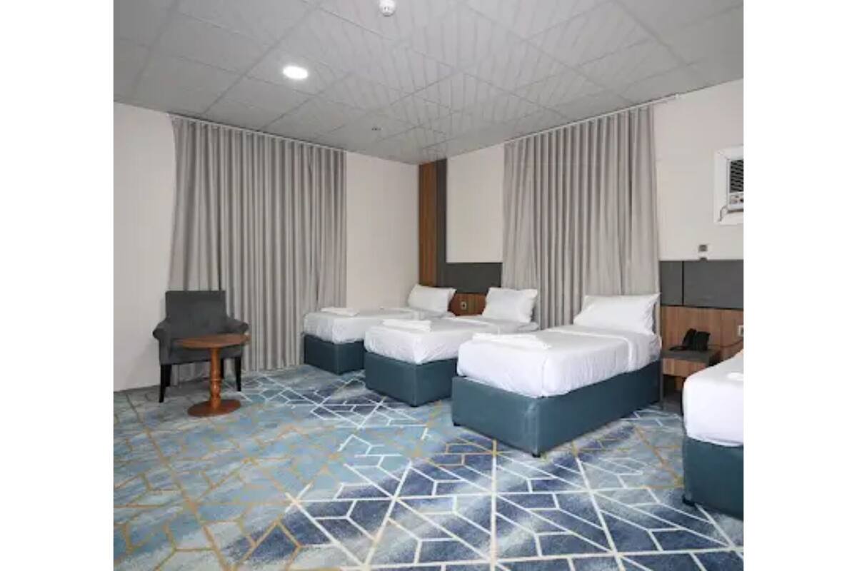 A hotel room with two beds, a chair, a small table, and a patterned floor.