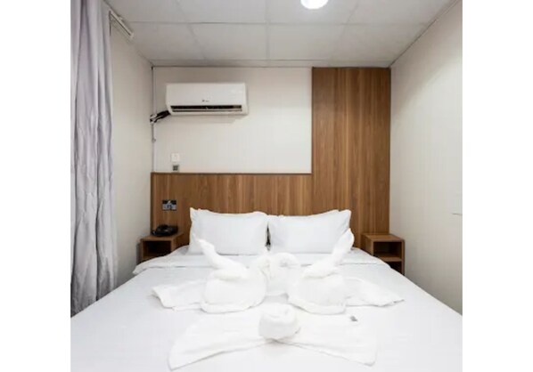 A hotel room with a bed, a wooden headboard, a nightstand, an air conditioning unit, and a curtain. - Wardat rahiq (Madinah)
