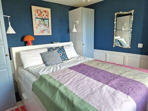 Quarto com cama, luminária de cabeceira, espelho e um quadro na parede.