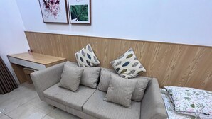 Un sofá de tonos neutros con cojines estampados, un cabecero de madera, una mesita de madera y una cama con ropa de cama floral.
