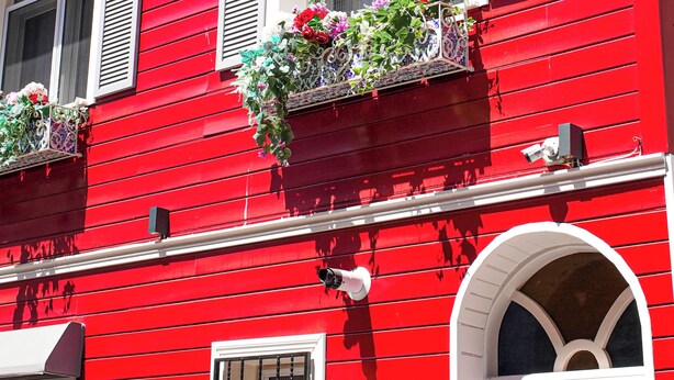 Ein rotes Gebäude mit zahlreichen Fenstern, von denen einige mit Fensterläden versehen sind, und Blumenkästen an den oberen Etagen.
