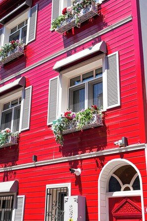 Un edificio rojo con muchas ventanas, algunas con contraventanas y jardineras en los pisos superiores.