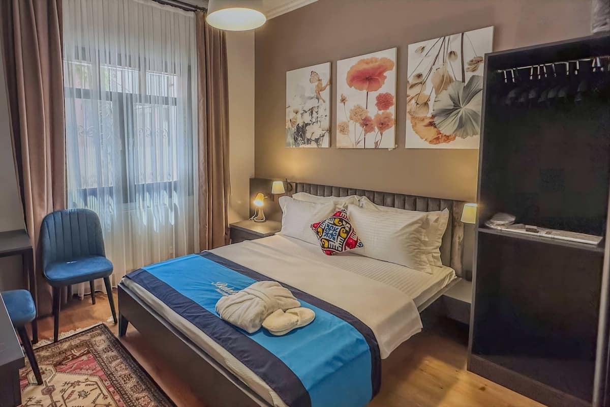 Quarto de hotel com cama, escrivaninha, cadeira, televisão e obras de arte na parede.