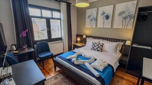 Ein Hotelzimmer mit Bett, Schreibtisch, Stuhl, einem Fenster mit Vorhängen und Wandbildern.