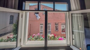 Vista a través de una ventana que muestra un edificio con múltiples ventanas y un balcón lleno de flores.